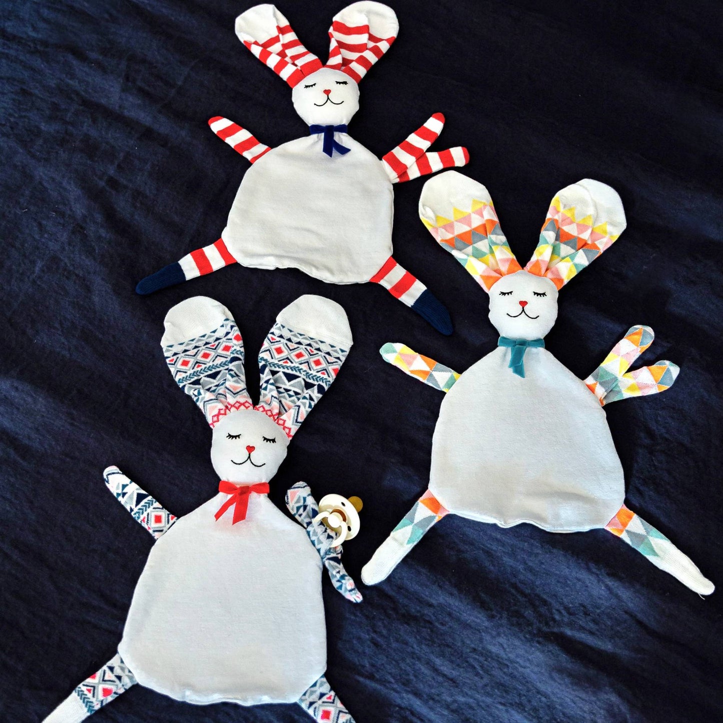 3 doudous plats lapins avec oreilles en chaussettes sur lit bleu par Sonia