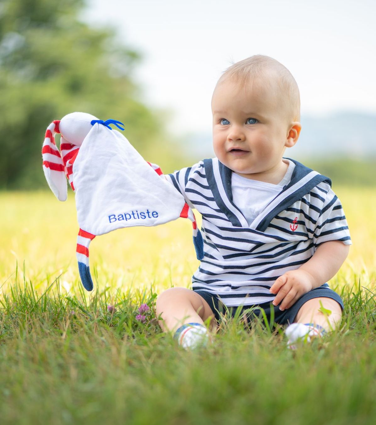 joli petit garçon joue dans l'herbe avec son doudou à rayures et longues et douces oreilles rouges et blanches
