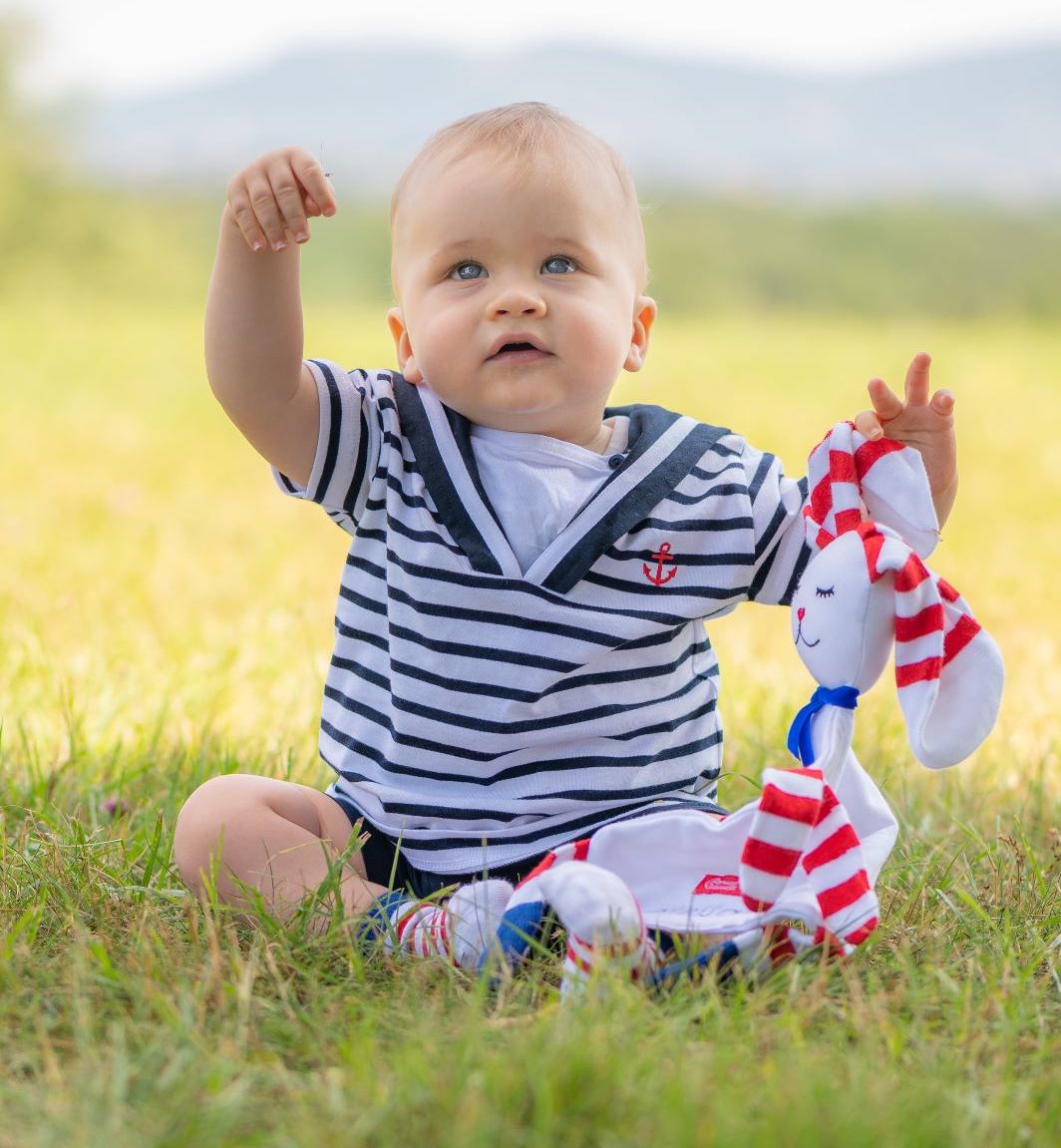 bebe mariniere joue avec un doudou lapin à rayures dans un jardin.jpg