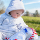 adorable bébé assis dans l'herbe avec capuche blanche qui regarde son doudou à rayures blanches et rouges