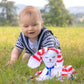 petit garçon blond de 6 mois qui joue avec un doudou lapin à rayures dans un jardin.jpg